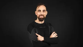 Lächender Mann mit gekreuzten Armen vor schwarzem Hintergrund. © Sport Kessler GmbH