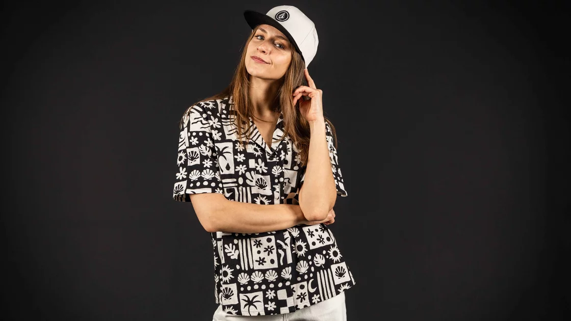 Woman wearing a black and white patterned shirt and a white baseball cap against a black background. © Sport Kessler GmbH