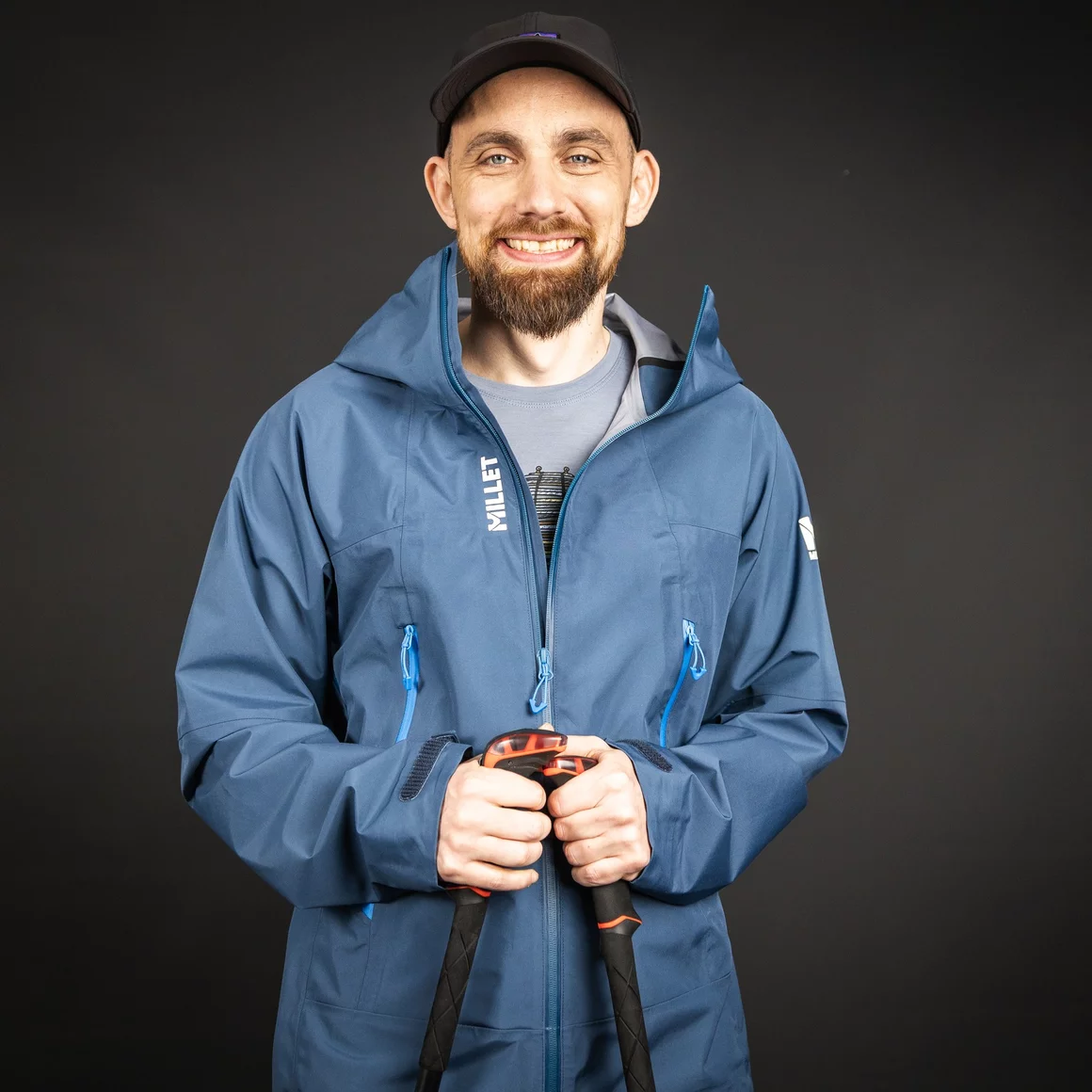 Lächelnder Mann in blauer Funktionsjacke mit Wanderstöcken. © Sport Kessler GmbH