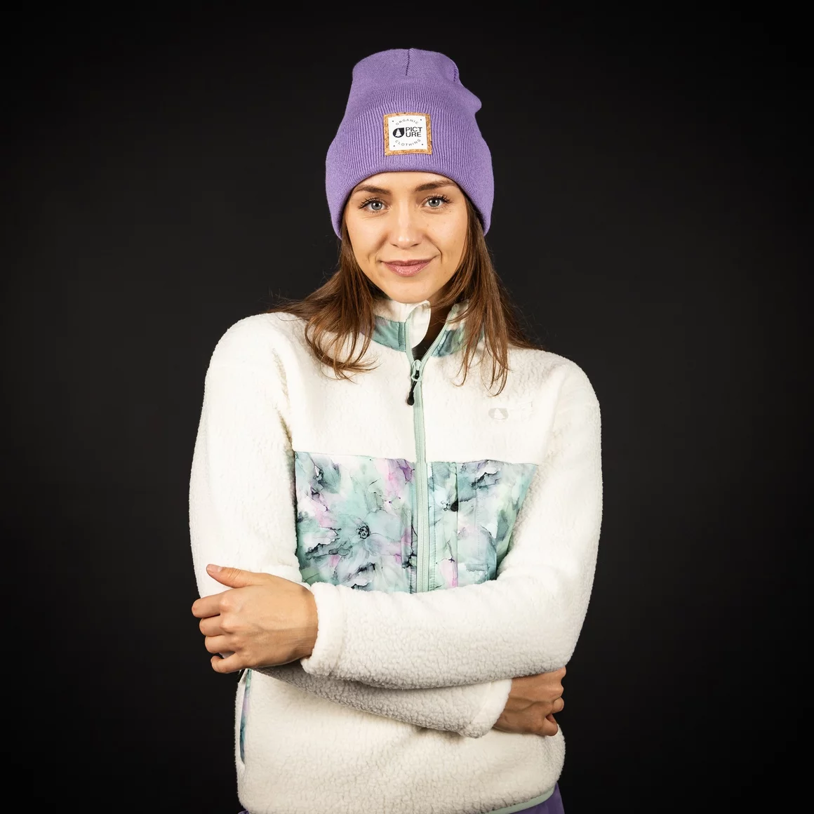 Woman wearing a purple beanie and a cream-colored fleece jacket with floral accents. © Sport Kessler GmbH