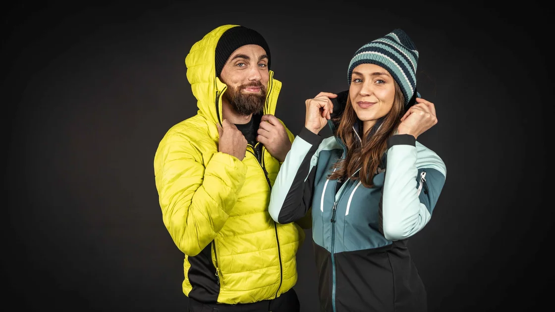 Mann und Frau in Winterkleidung vor dunklem Hintergrund. © Sport Kessler GmbH