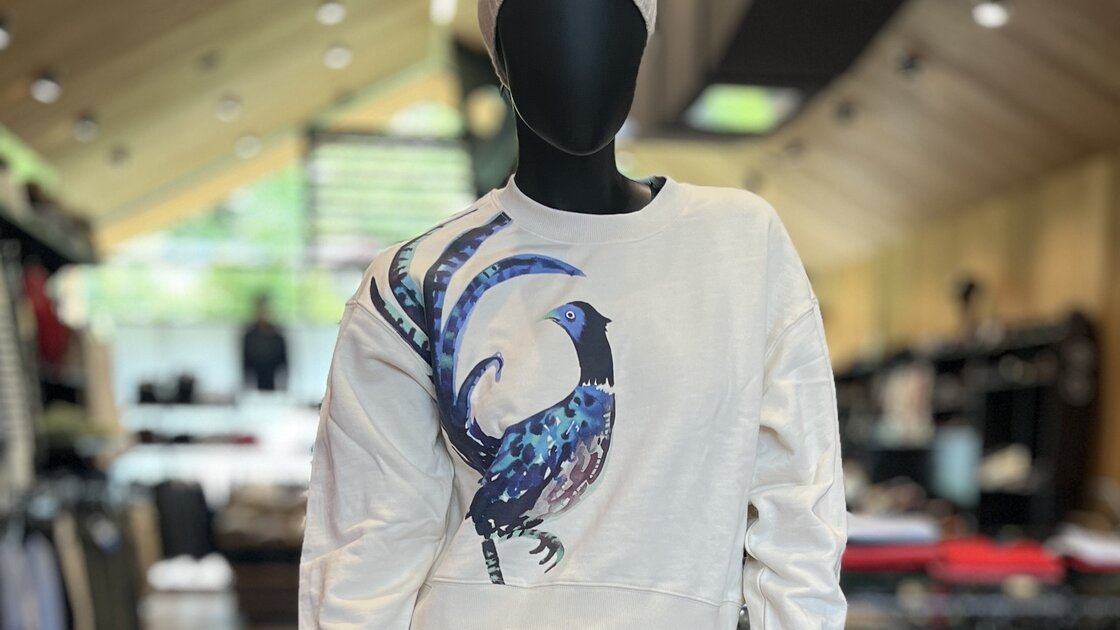 Mannequin in a cream sweatshirt with a blue bird graphic and denim jeans. © Sport Kessler GmbH
