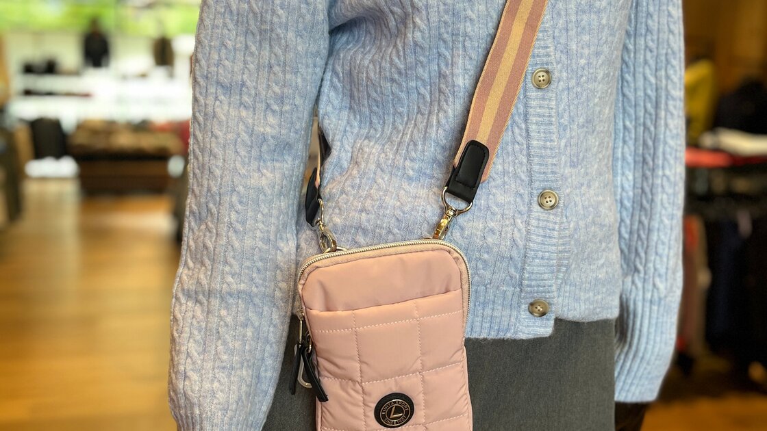 Mannequin showcasing a light blue cable-knit cardigan, pink crossbody bag, and grey trousers. © Sport Kessler GmbH