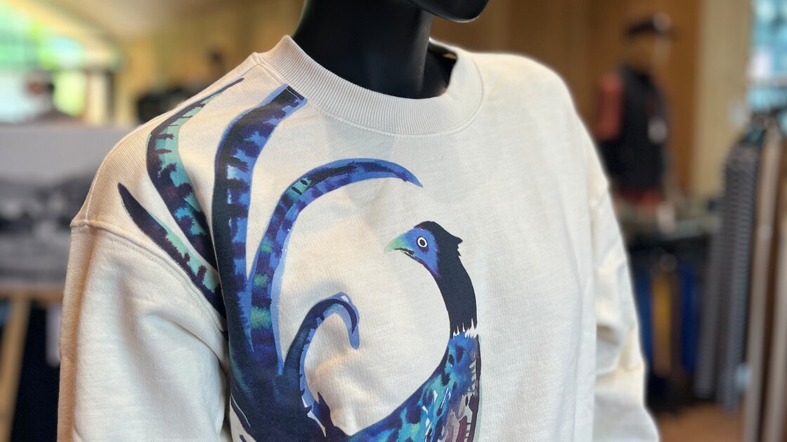 Cremefarbener Pullover mit blau-grünem Vogelmotiv auf Schaufensterpuppe. © Sport Kessler GmbH