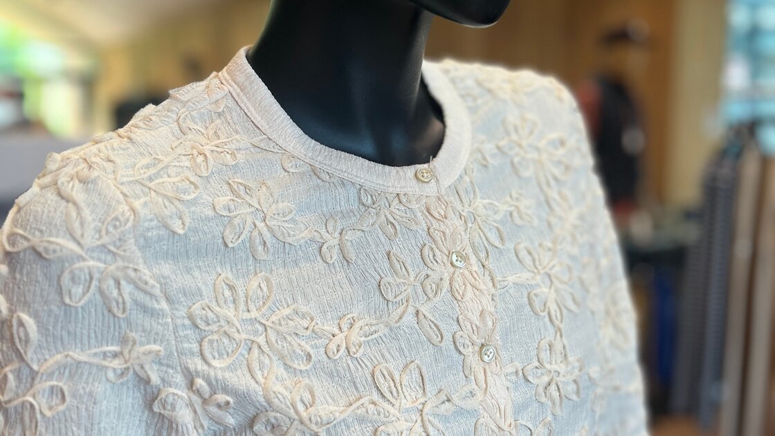 Elegantes Damenoberteil mit floralen Applikationen und passendem Strickhut. © Sport Kessler GmbH