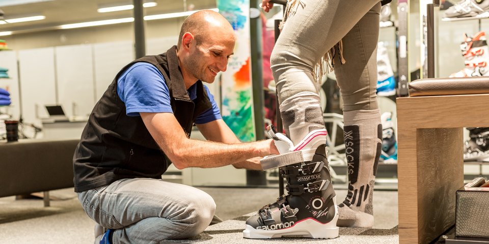 Verkäufer hilft Kundin beim Anziehen von Skischuhen. © Sport Kessler GmbH
