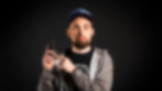 Man with a beard wearing a grey hoodie and cap, holding a phone and pointing at it with a dissatisfied expression. © Sport Kessler GmbH