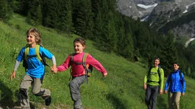 Zwei Kinder, Hand in Hand, rennen einen Bergweg entlang, während ihre Eltern ihnen folgen. © Sport Kessler GmbH