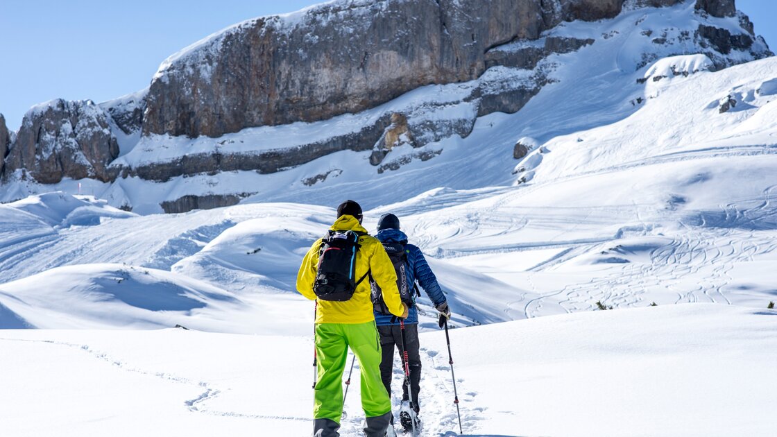 Zwei Schneeschuhwanderer mit leuchtend gelber und blauer Kleidung steigen in einer verschneiten Berglandschaft auf. © Kleinwalsertal Tourismus eGen