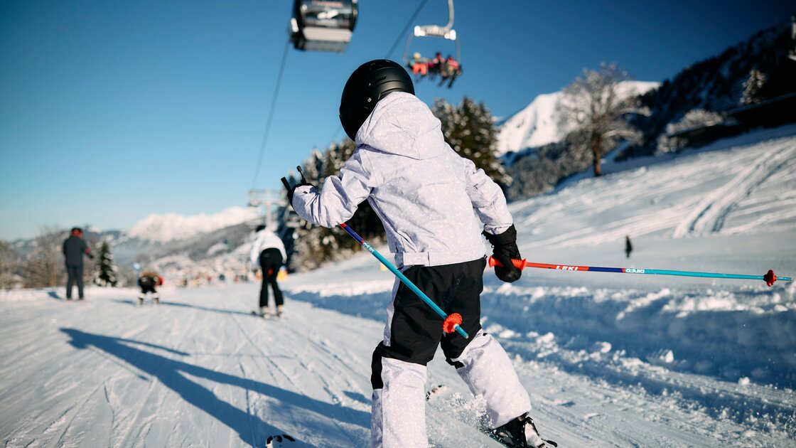 Skifahrer in heller Kleidung fährt bei Sonnenschein eine verschneite Piste hinunter. © Kleinwalsertal Tourismus eGen