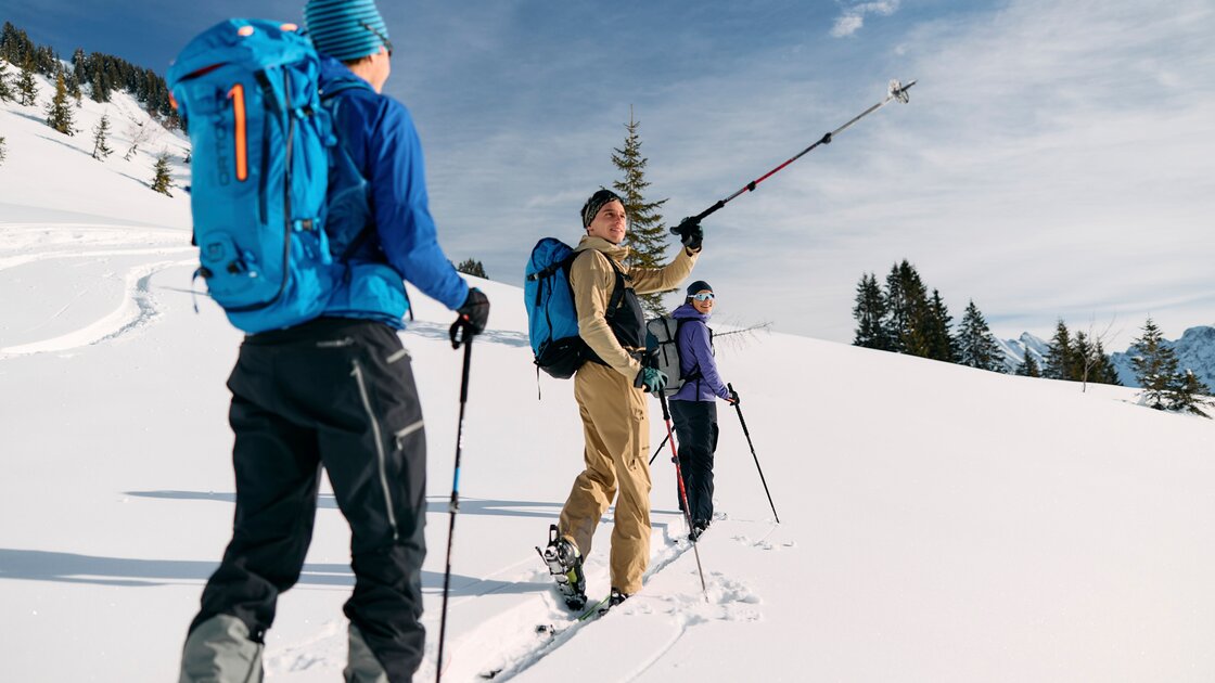 Drei Skitourengeher mit Rucksäcken wandern an einem sonnigen Tag durch tiefen Schnee in den Bergen. © Kleinwalsertal Tourismus eGen
