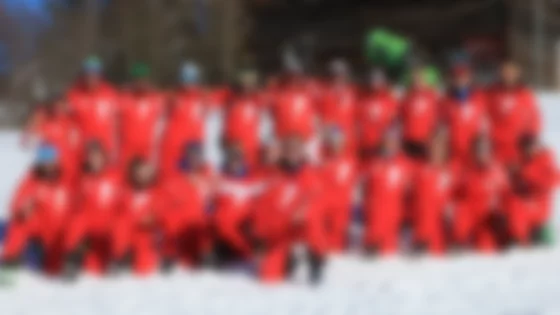 Eine Skilehrergruppe in roten Uniformen posiert im Schnee vor einem Holzhaus. © Skischule Seite Egg