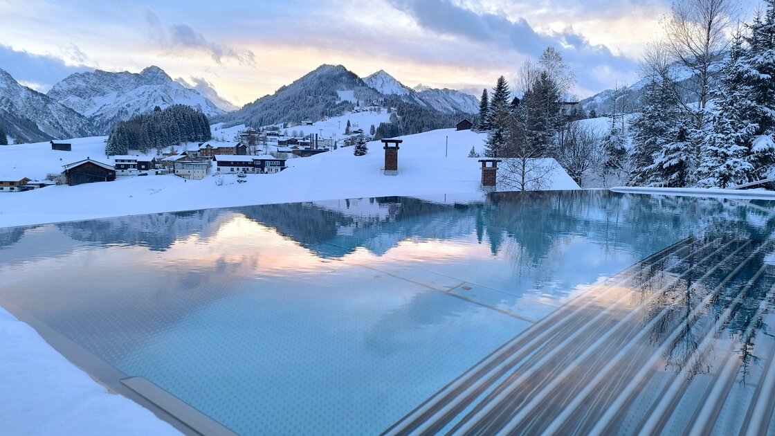 Infinity-Pool mit Spiegelung der verschneiten Alpenlandschaft und des Dämmerungshimmels. © Hotel Erlebach