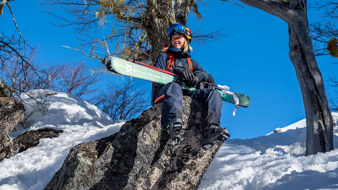 A woman skier rests on a rock, skis in hand, enjoying a sunny day in a snowy mountain landscape. © Marker Dalbello Völkl International GmbH