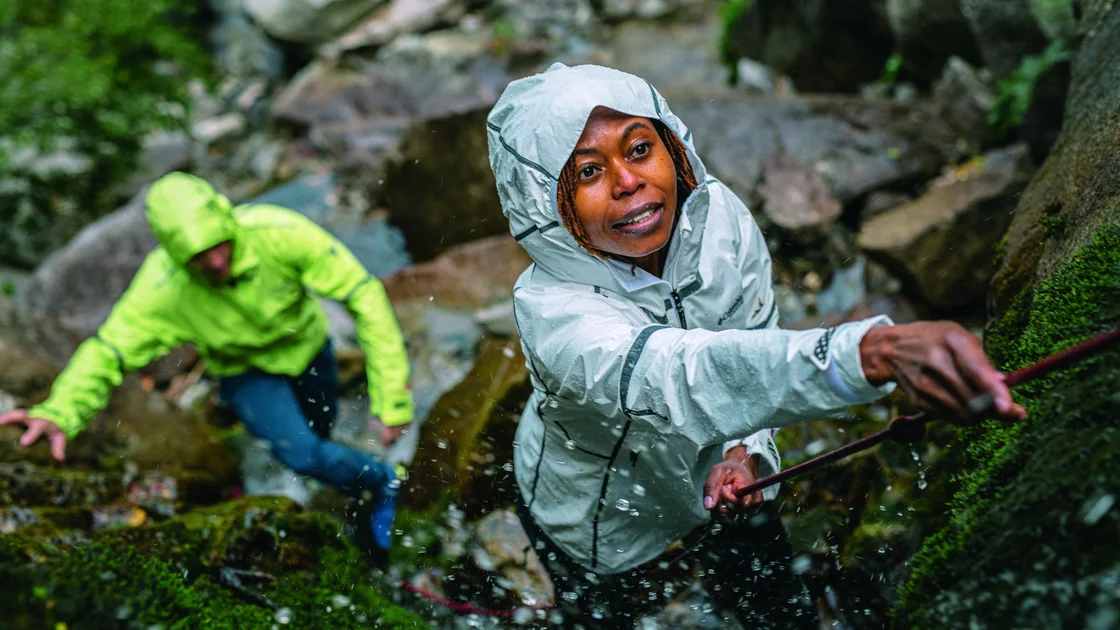 Zwei Wanderer überwinden einen felsigen Bachlauf, die Frau im Vordergrund hält sich an einem Seil fest. © Columbia Sportswear