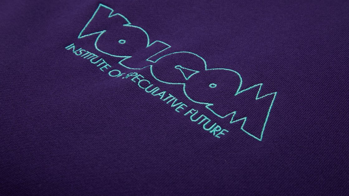 Nahaufnahme eines dunkelvioletten Stoffes mit einer helltürkisen Stickerei des Logos „Volcom Institute of Speculative Future“. © Sport Kessler GmbH